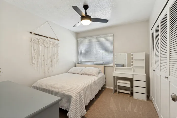 Neutral wall paint, ceiling fan with integrated lighting, window with horizontal blinds, and carpeted flooring