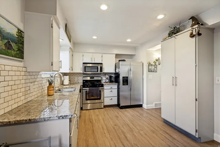 Kitchen featuring white cabinetry, stainless steel appliances, granite countertops, subway tile backsplash, and wood-finish flooring