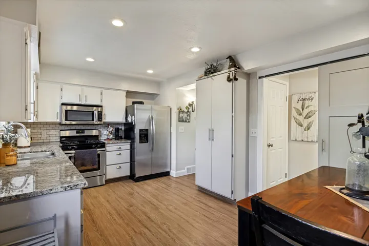 Kitchen featuring white cabinetry, stainless steel appliances, speckled countertops, and wood-finish flooring