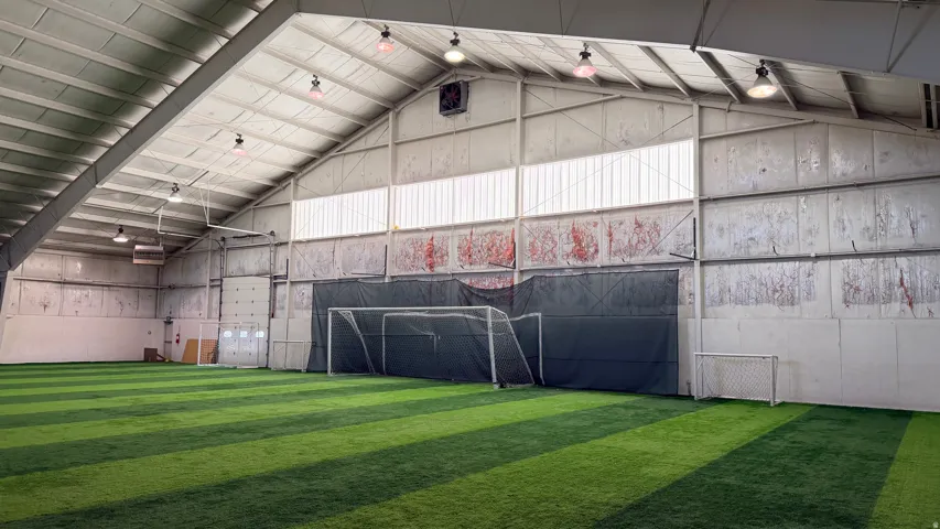 Expansive indoor facility featuring artificial turf flooring, high ceilings with exposed structural beams, and integrated lighting fixtures