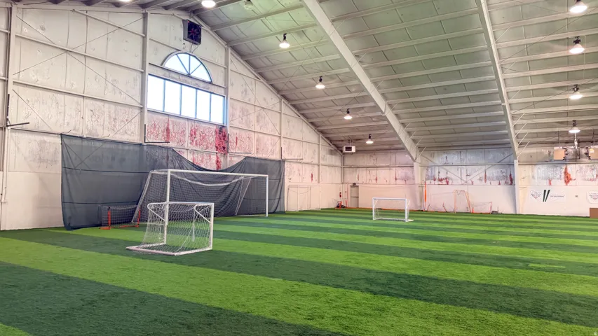 Expansive indoor turf field with high vaulted ceilings and ample overhead lighting
