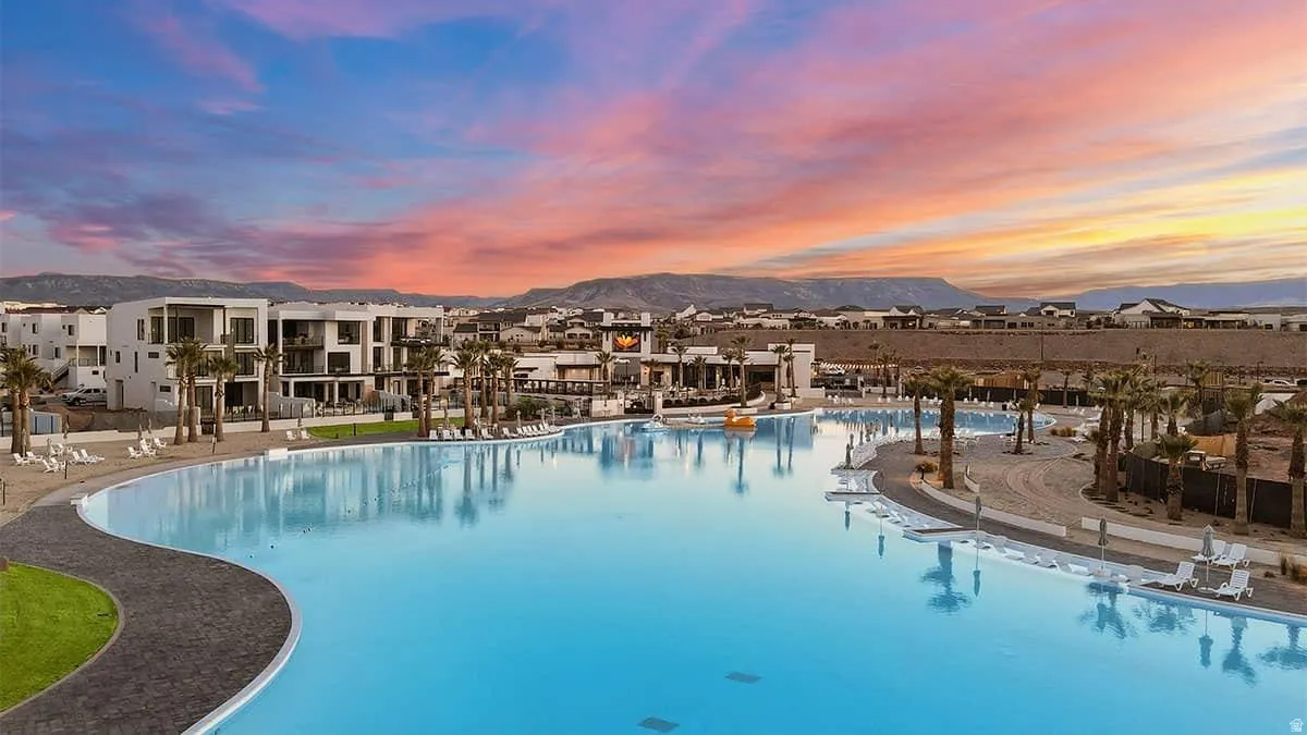 Expansive turquoise lagoon surrounded by contemporary multi-story buildings, multiple palm trees, and mountain scenery