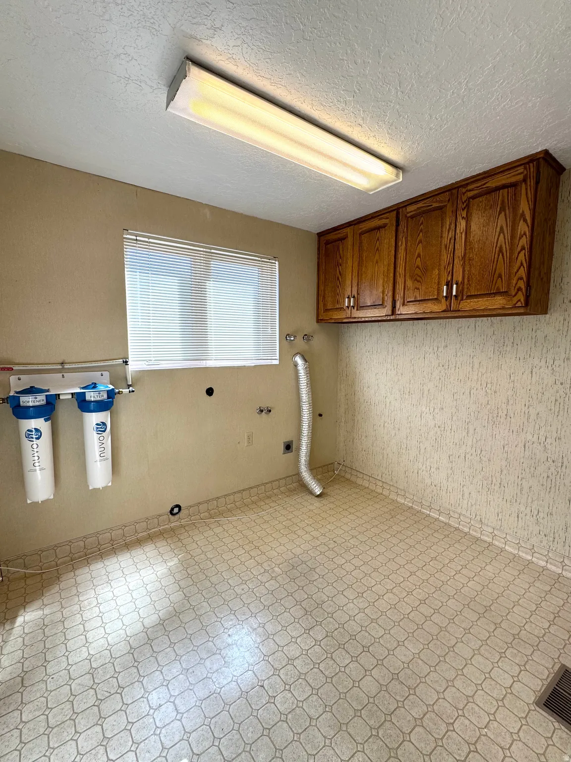 Utility room with patterned flooring, overhead lighting, and wood-finish cabinetry