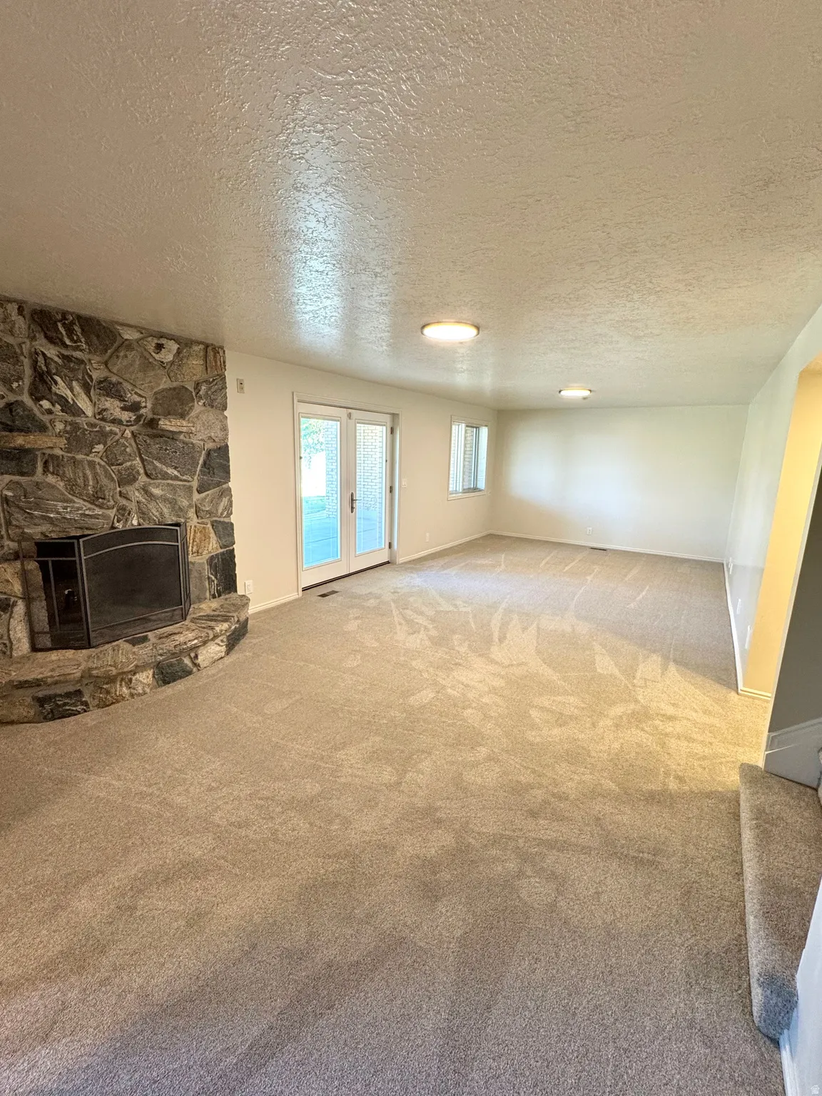 Stone-clad fireplace, light-toned carpeting, white walls, double French doors, and recessed ceiling lighting