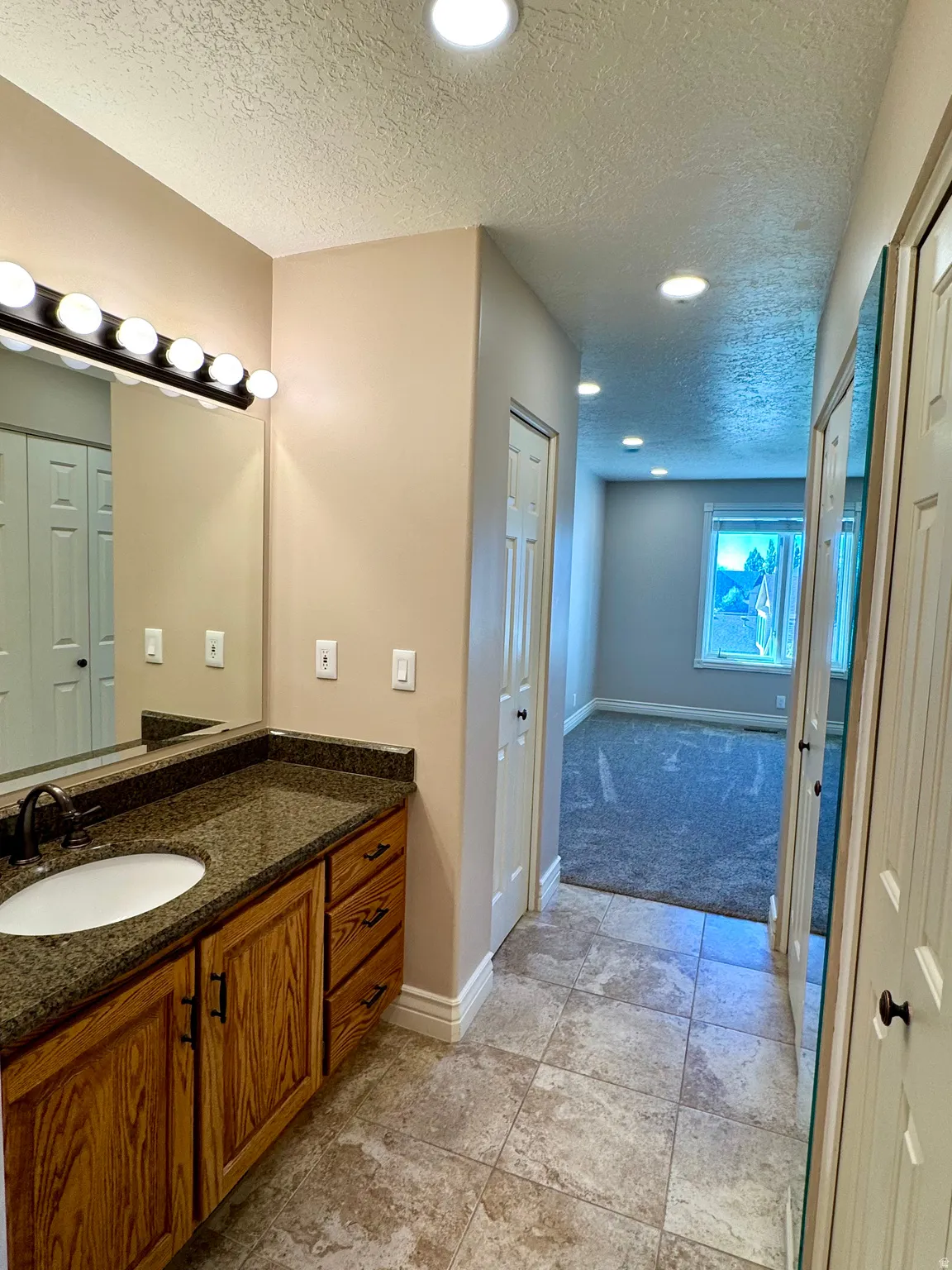 Wood-finish vanity with an integrated sink and dark countertop, full-width vanity mirror, tile flooring, and recessed ceiling lighting