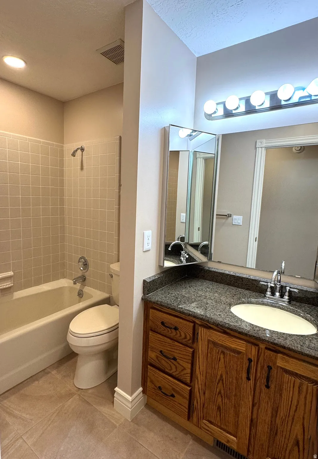 Wood-finish vanity with a dark speckled countertop, undermount sink, and chrome fixtures