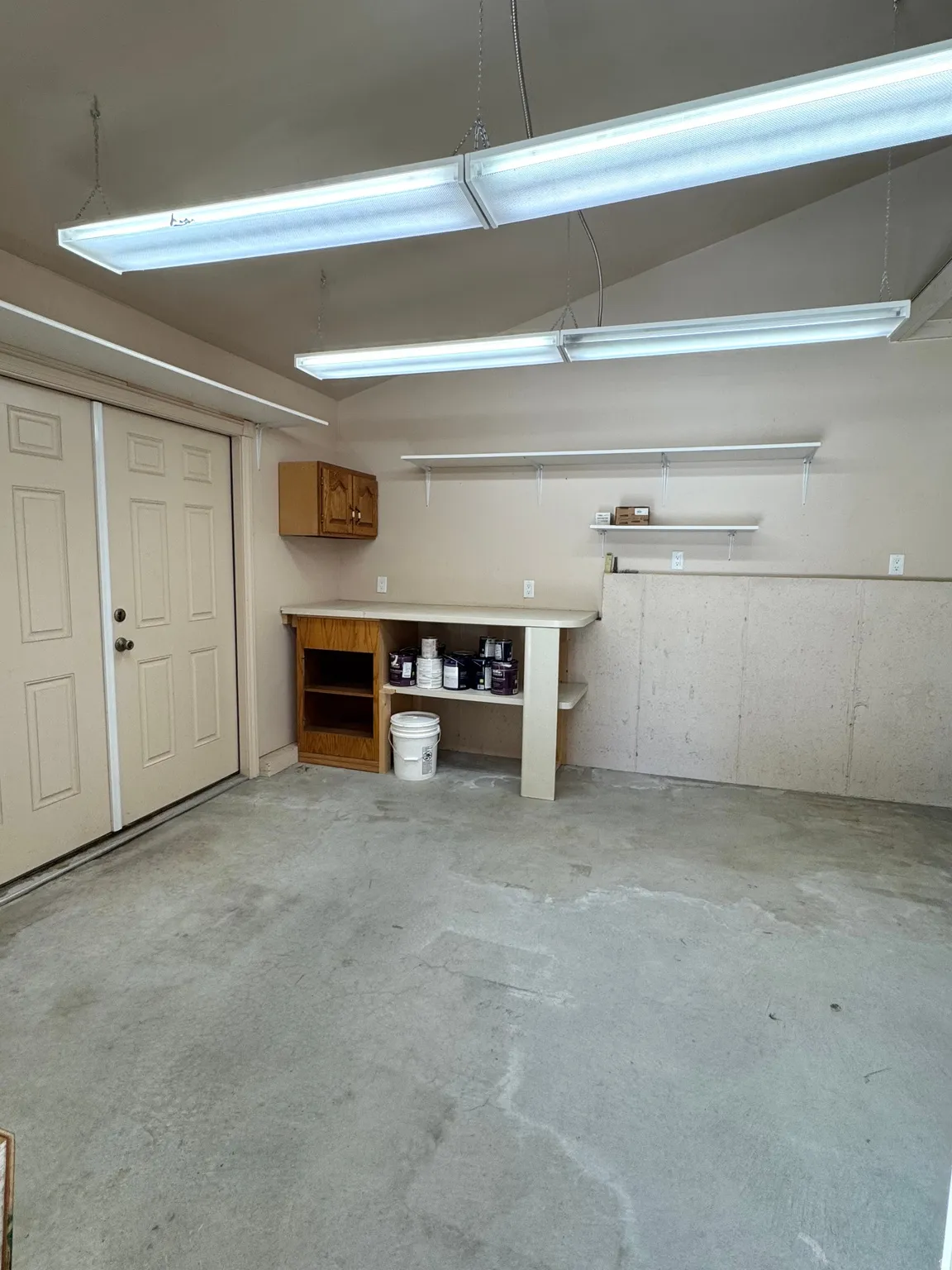 Concrete flooring, built-in workbench, wall-mounted shelving, built-in cabinetry, overhead fluorescent lighting