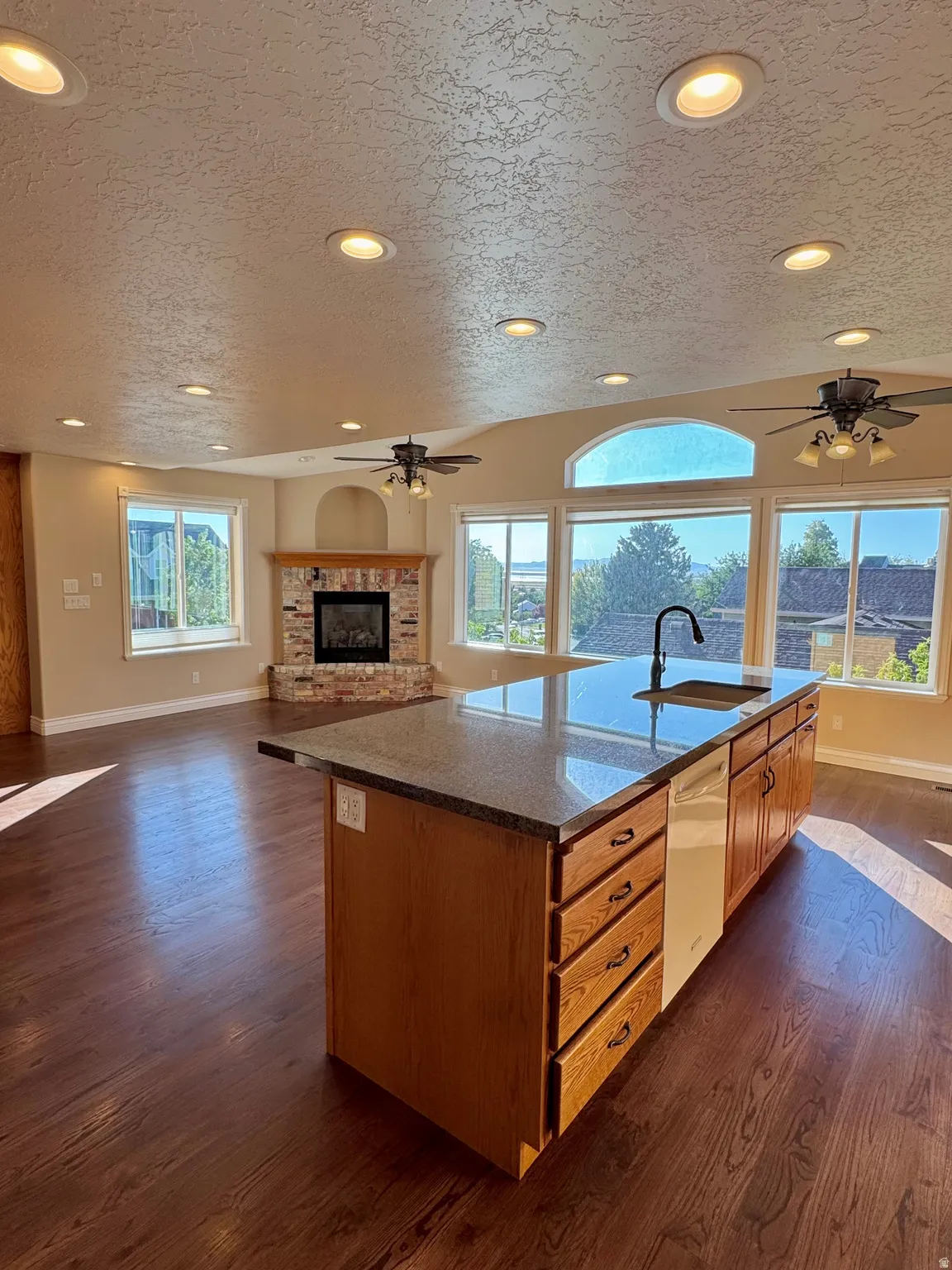 Kitchen island with a built-in sink, wood-finish flooring, recessed lighting, and a brick-faced fireplace