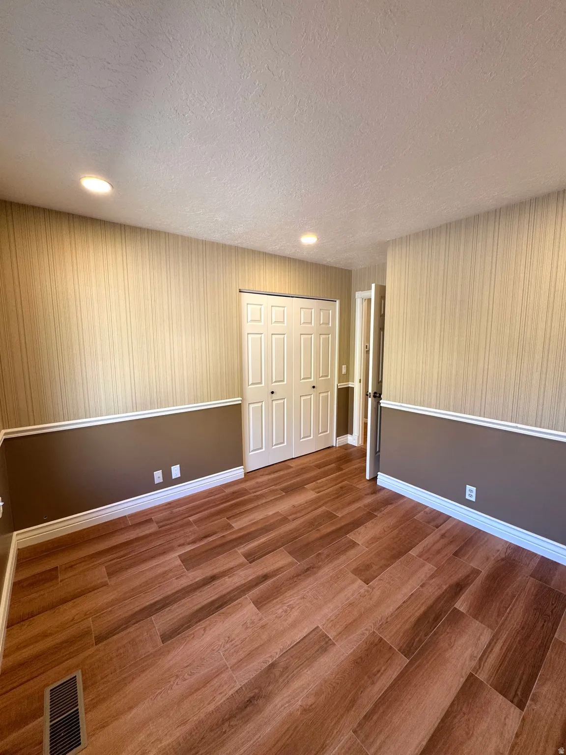 Wood-finish flooring, recessed lighting, crown molding, two-panel bifold closet doors, and wall trim with chair rail detailing
