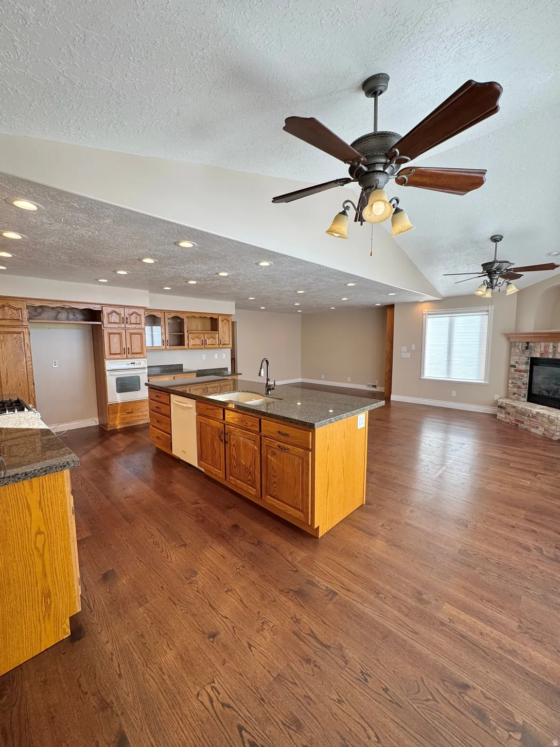 Spacious open-concept living area featuring wood-finish flooring, recessed lighting, ceiling fans, and a kitchen island with stone countertops