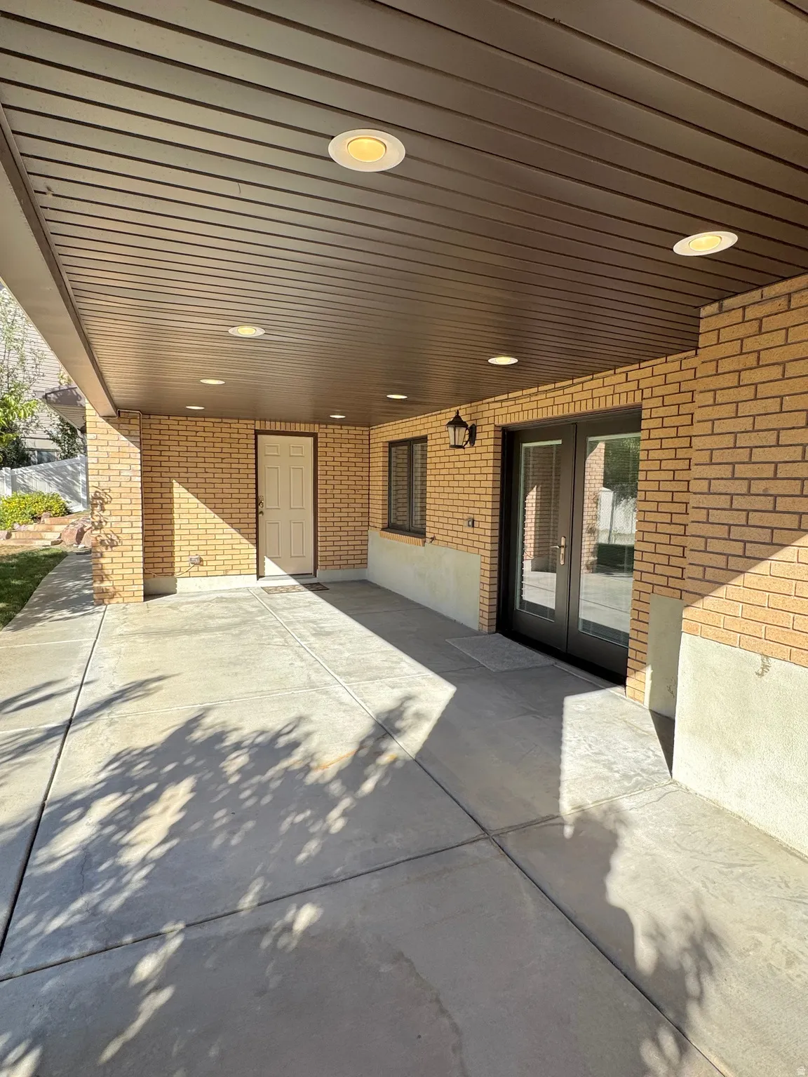 Covered patio area featuring a concrete surface, brick wall accents, recessed lighting, and double glass doors