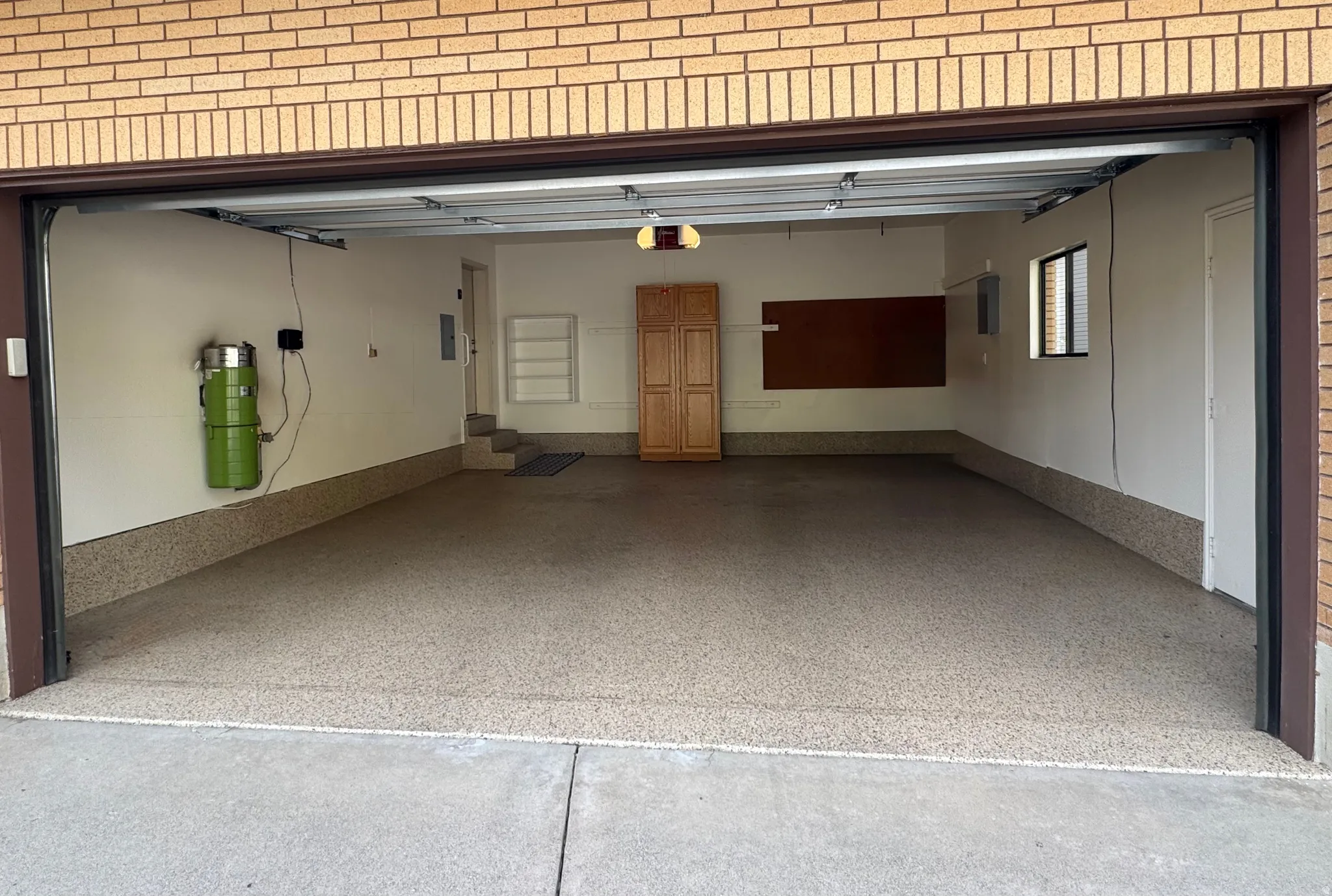 Spacious garage featuring a durable epoxy floor coating, built-in wooden cabinetry, and a central vacuum system