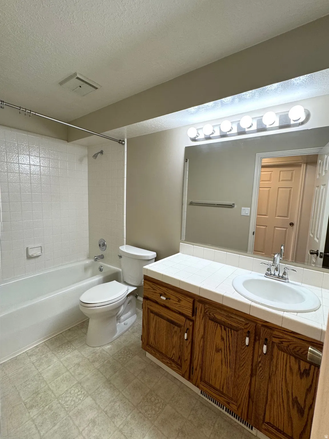 White tiled shower-tub combination, wood-finish vanity with ample storage, white tile countertop, integrated sink, and large vanity mirror