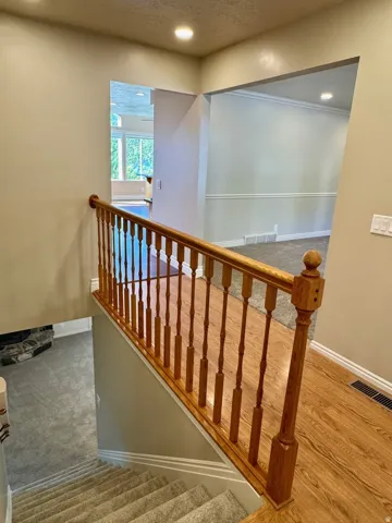 Staircase featuring wood-finish flooring, carpeted steps, and a wooden banister