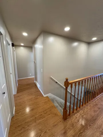 Hallway featuring wood-finish flooring, recessed lighting, and a wood banister with a white handrail