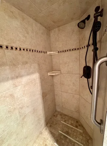 Tiled shower with decorative accent border, built-in corner shelving, and a dark bronze shower fixture