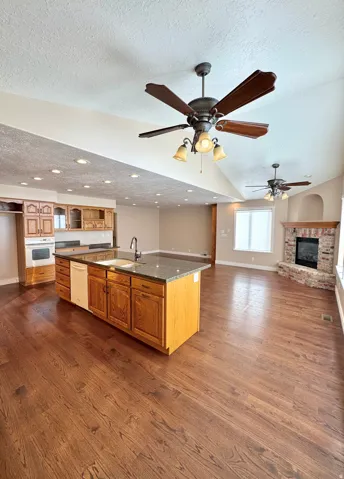 Open-concept living space featuring wood-finish flooring, a kitchen island with stone countertop, recessed lighting, and a brick-surround fireplace