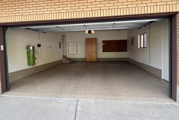 Spacious garage featuring a durable epoxy floor coating, built-in wooden cabinetry, and a central vacuum system