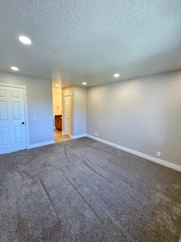 Spacious room featuring plush gray carpeting, recessed ceiling lighting, and light-toned wall paint