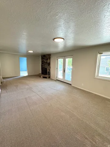 Textured ceiling, recessed lighting, stone fireplace, French doors, carpet flooring