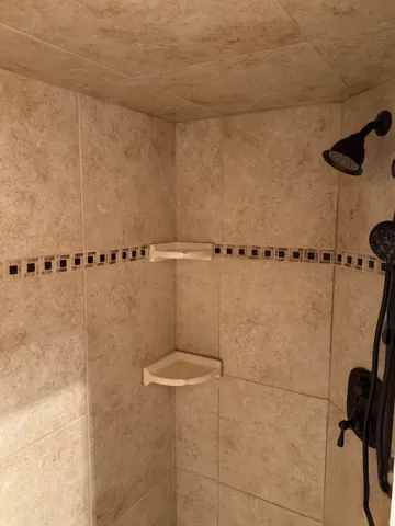Tiled shower enclosure with a decorative mosaic accent band, two corner shelves, and a bronze-finish showerhead