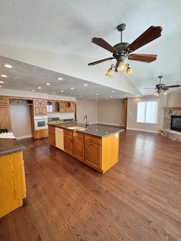 Spacious open-concept living area featuring wood-finish flooring, recessed lighting, ceiling fans, and a kitchen island with stone countertops