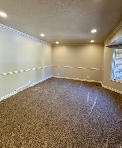 Recessed ceiling lighting, crown molding, chair rail molding, carpet flooring, and a bay window
