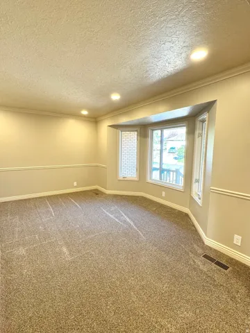 Recessed ceiling lighting, crown molding, textured walls, bay window, and carpeted flooring