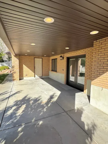 Covered patio area featuring a concrete surface, brick wall accents, recessed lighting, and double glass doors