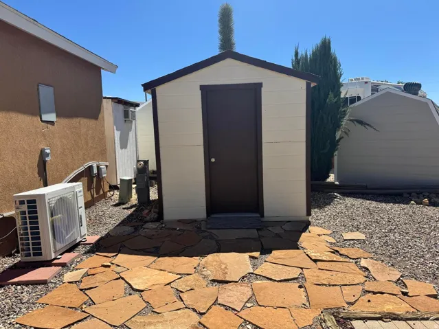 Neutral-toned shed with a dark brown door, situated on a flagstone path, surrounded by decorative gravel