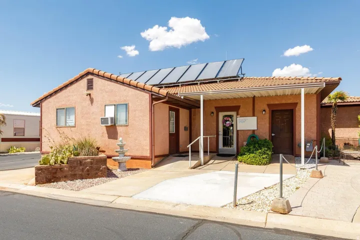 Stucco exterior building with a tile roof, featuring solar panels, multiple entryways, and a concrete ramp