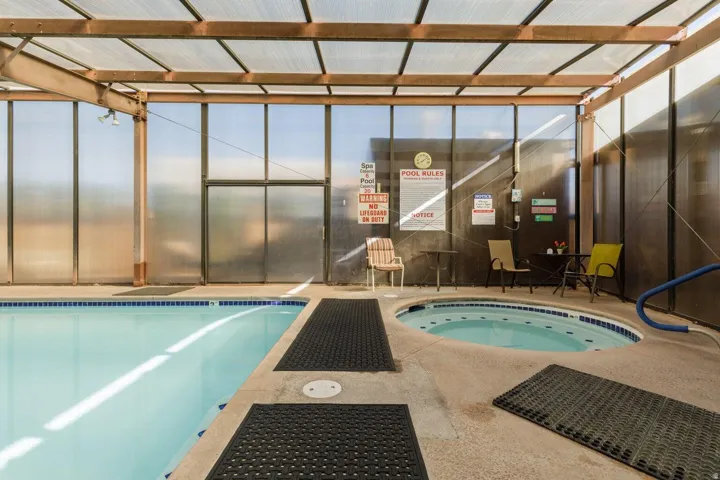 Indoor swimming pool with concrete decking, a built-in spa, and a translucent roof structure