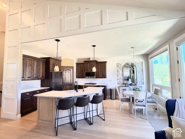 Kitchen featuring dark wood cabinetry, light countertops, a central island with seating, pendant lighting, and light laminate flooring
