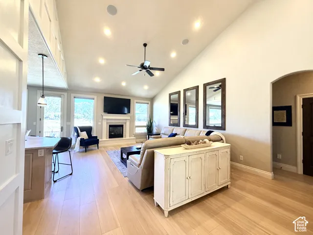 Vaulted ceilings with recessed lighting, fireplace with mantel, light laminate flooring, and arched doorway