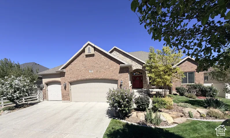 Brick exterior with a stone accent facade, featuring a red arched entryway, two attached garages, a concrete driveway, and landscaped rock gardens