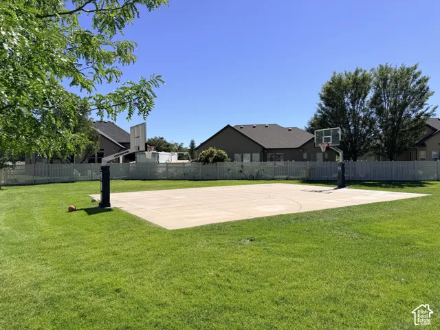Expansive green lawn with a concrete sports court and two basketball hoops, enclosed by a white privacy fence