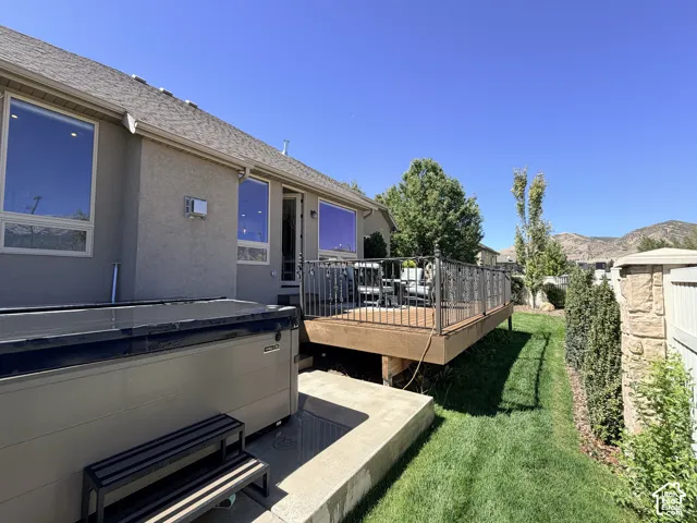 Raised wood-finish deck with ornate metal railing, private hot tub, and stucco exterior