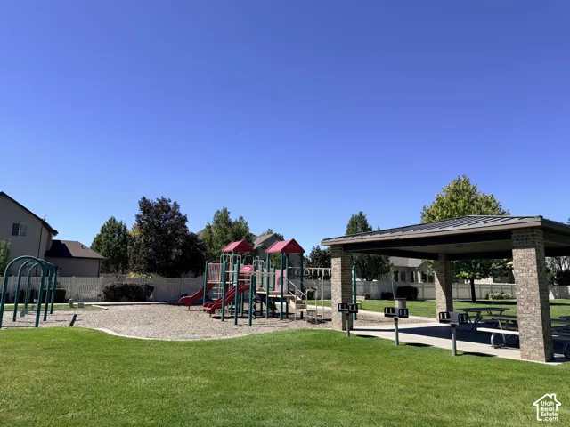 Community green space featuring a covered picnic pavilion with built-in grills, a playground structure with slides, monkey bars, and swings, and a manicured lawn