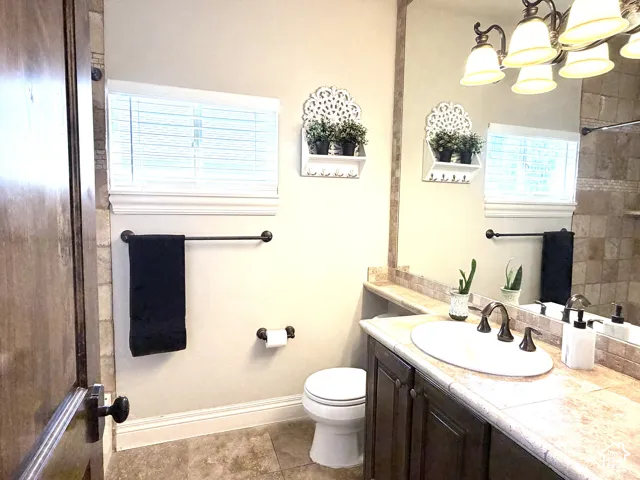 Full-height vanity mirror, dark wood-finish cabinetry, tile countertop, vessel sink with bronze-finish faucet, and coordinating wall-mounted light fixture