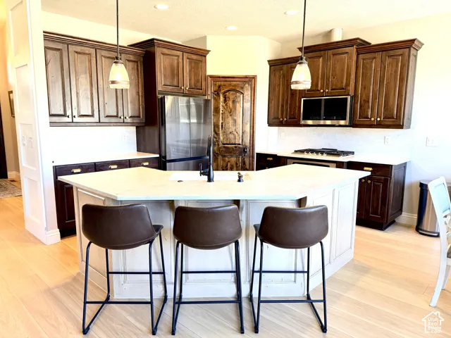 Kitchen featuring a light-toned island with a white countertop, dark wood-finish cabinetry, stainless steel appliances, a built-in microwave, and pendant lighting