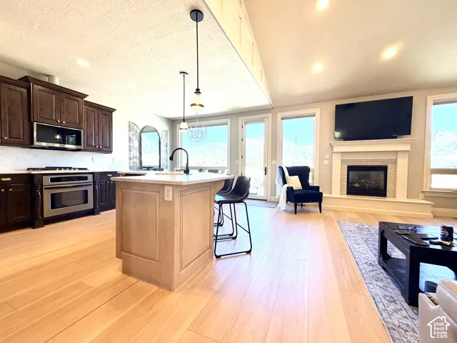 Open-concept living space with light laminate finish flooring, a built-in fireplace, and a kitchen island with pendant lighting