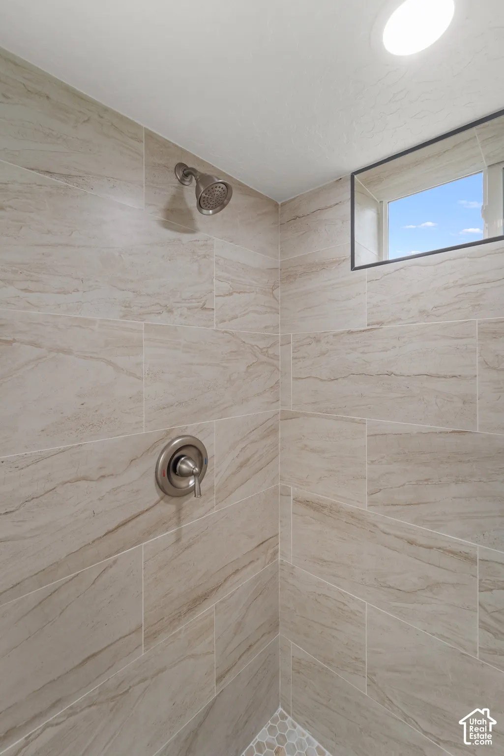 Shower featuring large format wall tiling, a circular overhead light, and a window for natural illumination