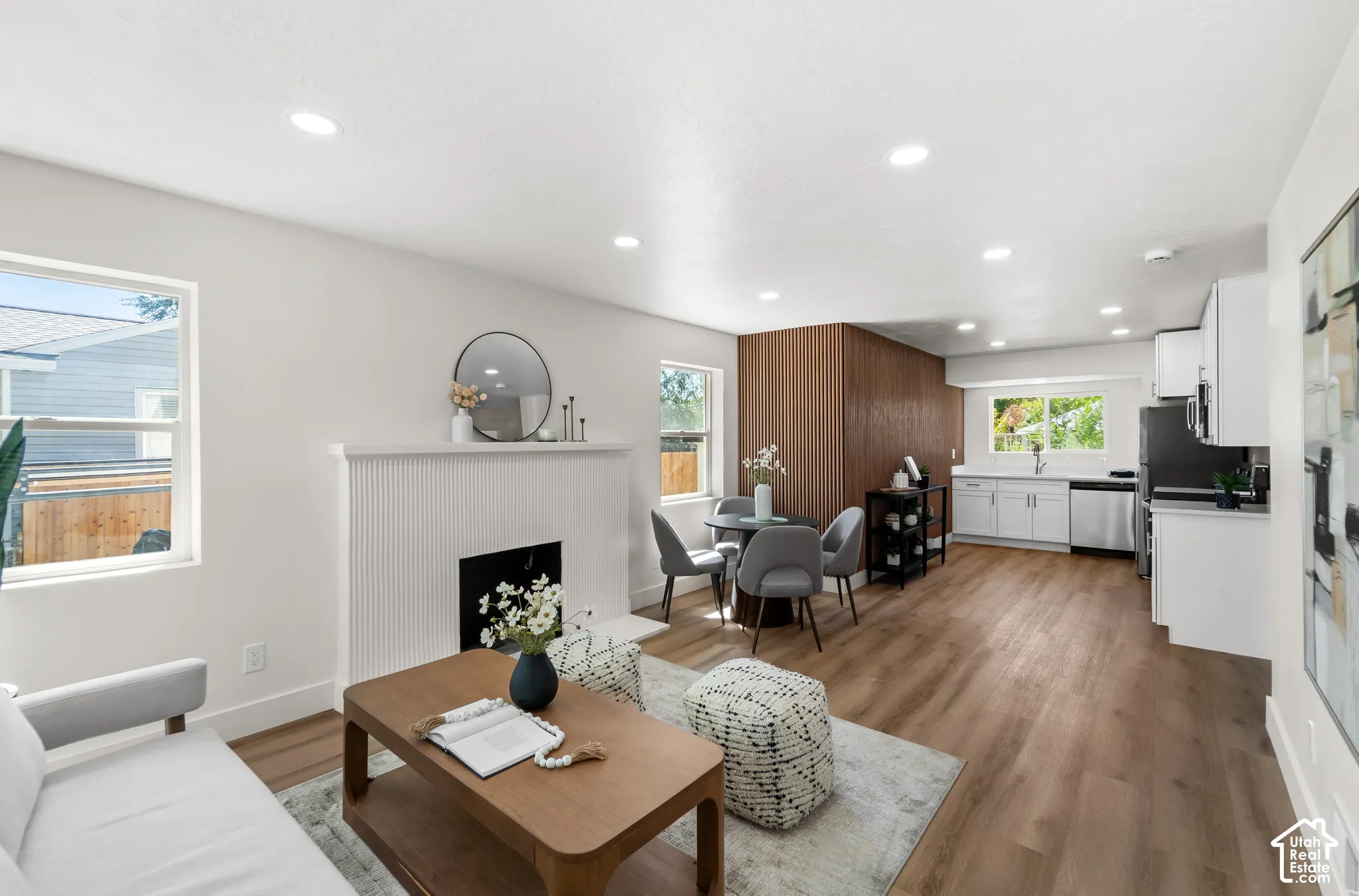 Open-concept living space featuring wood-finish flooring, recessed lighting, a decorative fireplace, and a kitchen with stainless steel appliances and white cabinetry