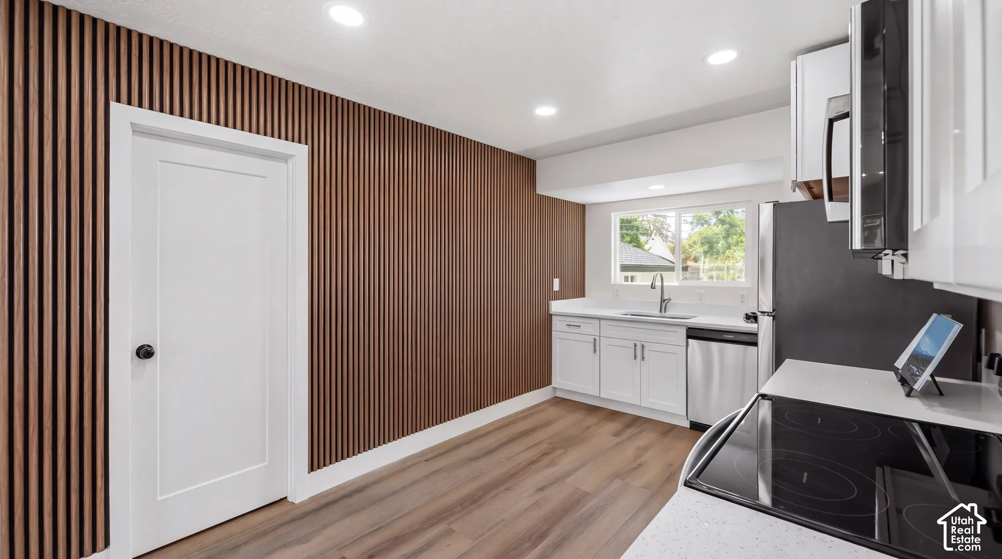 Contemporary kitchen with wood-finish accent wall, wood-finish flooring, recessed lighting, white cabinetry, and stainless steel appliances