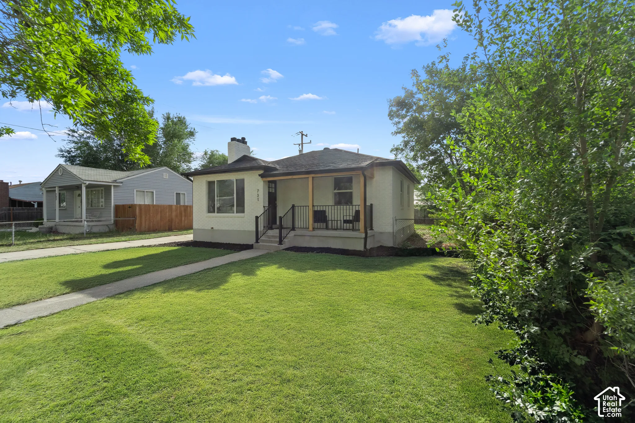 Single-story residence with a covered porch, front yard, concrete walkway, and established trees