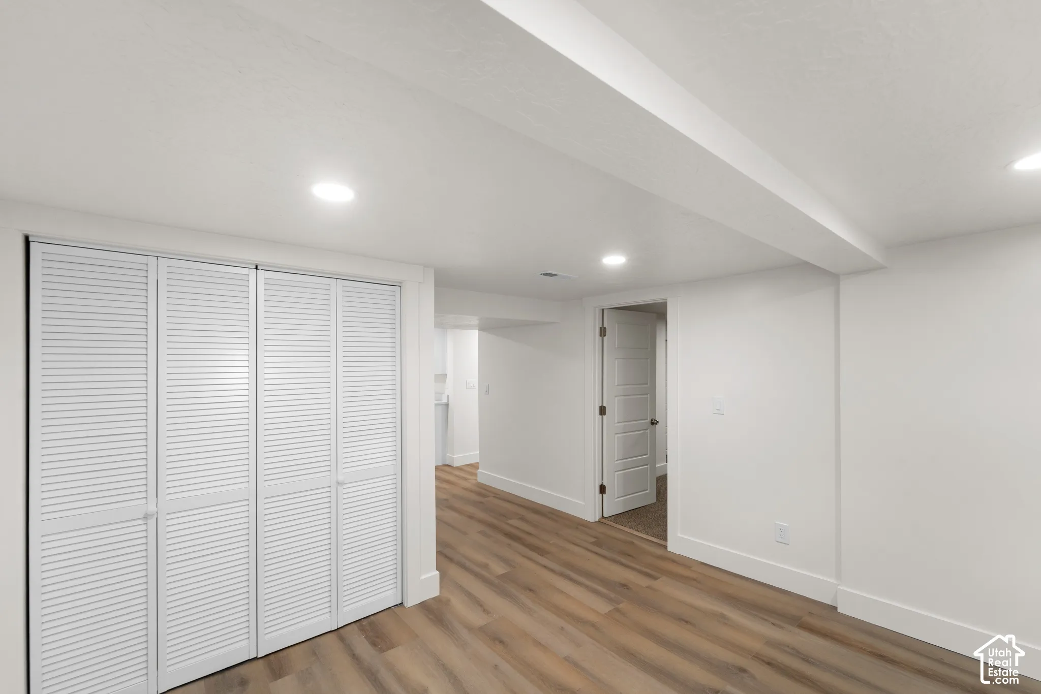 White louvered bifold closet doors, recessed lighting, wood-finish flooring, and white interior doors