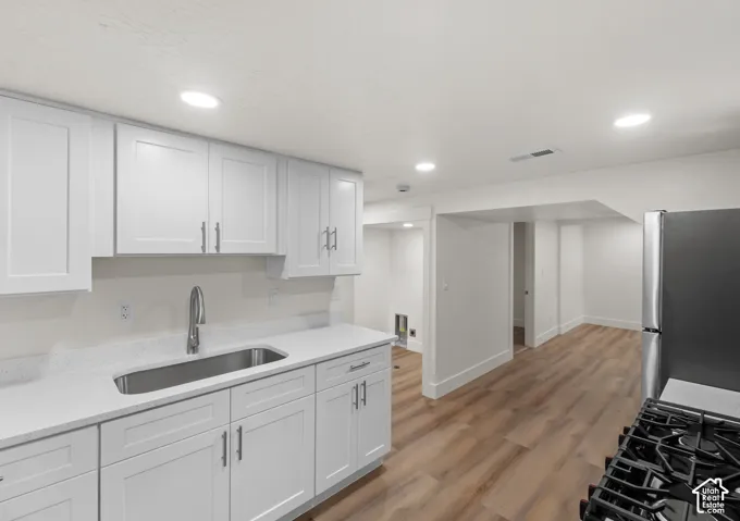 Modern kitchen featuring white shaker cabinetry, stainless steel sink with a gooseneck faucet, light-toned countertops, wood-finish flooring, and recessed lighting