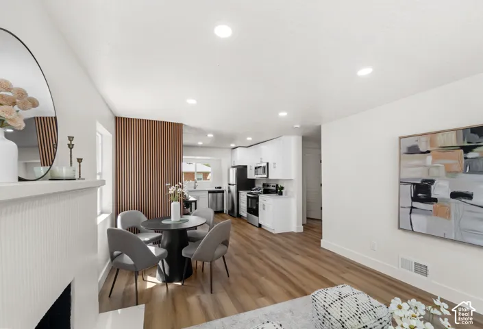 Integrated kitchen and dining area, wood-finish flooring, recessed lighting, white cabinetry, and stainless steel appliances