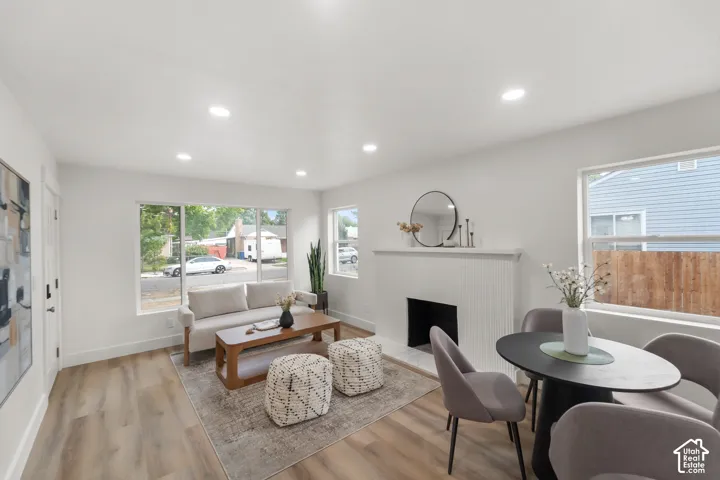 Recessed ceiling lighting, wood-finish flooring, white painted walls, white fireplace with hearth, and large windows