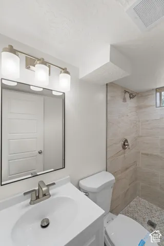 Vanity with an integrated sink and brushed nickel faucet, mirror with a black frame, three-light vanity fixture with frosted glass shades, shower with light-toned tile walls and a pebble-tiled floor